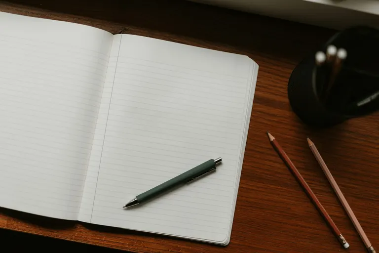 Een open, leeg notitieboek met een groene pen op een houten bureau in daglicht.